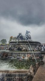 Fountain in park against cloudy sky