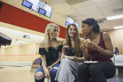 Three young women eatnig at a bowling alley.