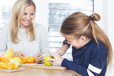 Mother and daughter cutting fruits on table at home