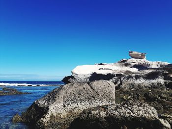 View of a rock by sea against clear blue sky
