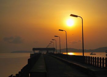 Street light by sea against sky during sunset