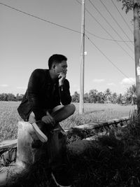 Full length of young man sitting on field against sky