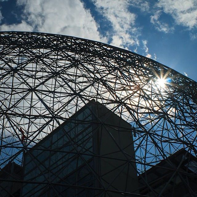 low angle view, built structure, architecture, sky, building exterior, sun, cloud - sky, sunbeam, modern, tall - high, glass - material, sunlight, tower, city, lens flare, cloud, day, no people, architectural feature, blue