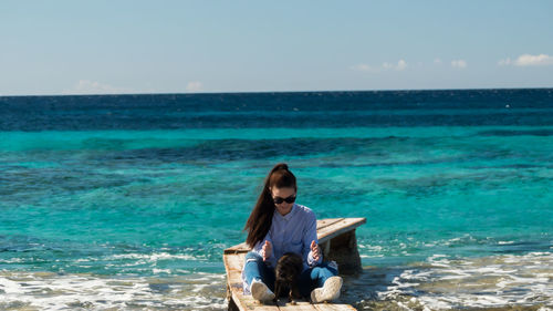 Woman sitting on beach against sky