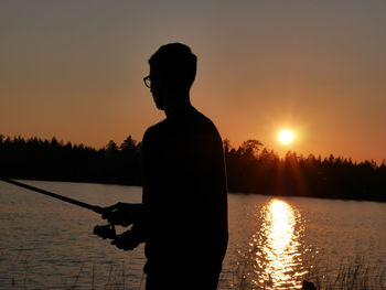 Silhouette man fishing in lake against clear sky during sunset