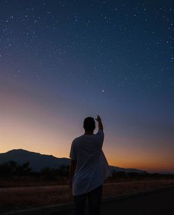 Rear view of man standing on field against sky at night