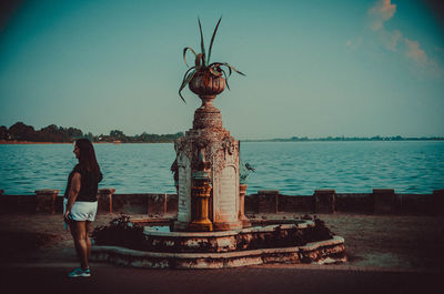 Rear view of woman standing by sea against clear sky