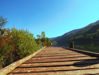 Wooden walkway by lake against clear blue sky