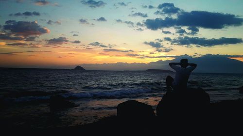 Silhouette woman standing on rock against sea during sunset