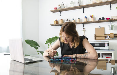 Female graphic designer using netbook and tablet with stylus while working on project at table in creative studio