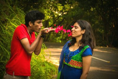 Happy young woman holding red rose against trees