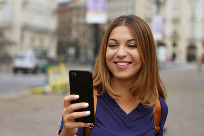 Portrait of smiling woman holding smart phone on street