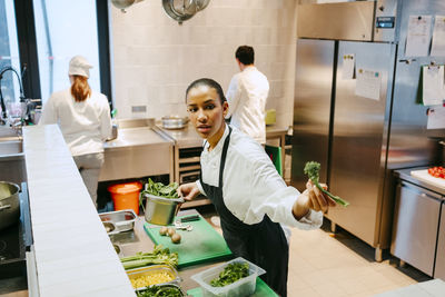 Young female chef holding vegetables while working in commercial kitchen