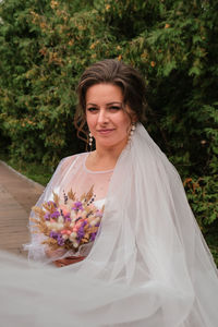 Beautiful smiling bride in traditional white wedding dress holding bouquet of dry homemade flowers. 