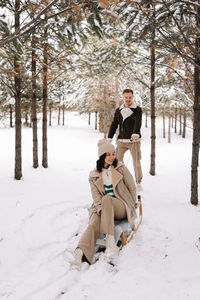 A man and a woman in love have fun and ride a sleigh in the forest among trees in winter in nature