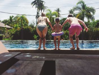 Rear view of parents holding daughter hands while diving in swimming pool during sunny day