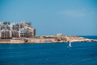 Buildings in sea against blue sky