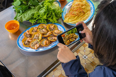 Woman taking photo and eating banh khot, vietnamese pancake