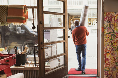 Rear view of owner carrying rolled up carpet while walking at store entrance