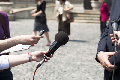 Cropped hands holding microphones towards businessman