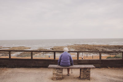 Rear view of woman sitting on bench at sea against sky