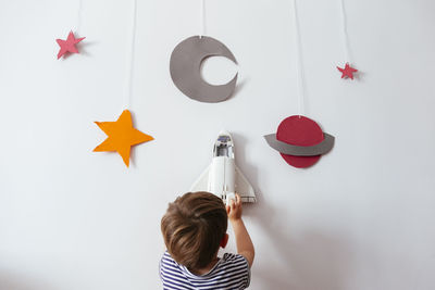 Rear view of boy holding toy rocket over wall with galaxy decoration