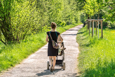 Rear view of woman with baby stroller walking on footpath 