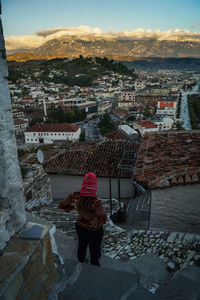 Rear view of woman standing against cityscape during sunset