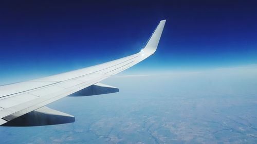 Cropped airplane flying over landscape against blue sky