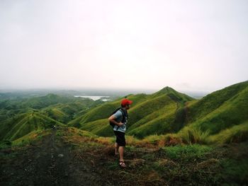 Side view of young man with backpack standing on mountain against sky