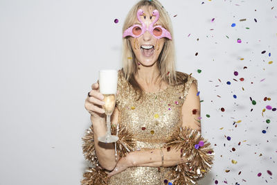 Senior woman wearing golden dress and flmingo shaped glasses, celebtraing new year's eve