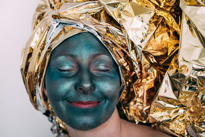 Close-up of woman with green facial mask wearing golden foil