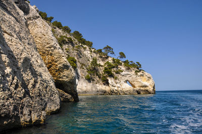 Rock formations by sea against clear blue sky