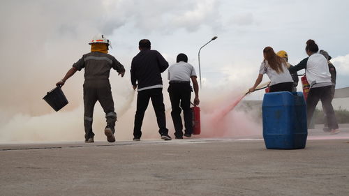 Rear view of people spraying water on fire against sky