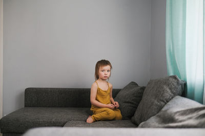 Cute sad european child sits alone on couch in real living room