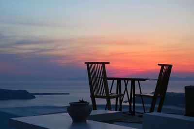 Chairs and table by sea against sky during sunset
