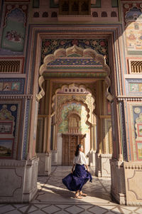 Cheerful ethnic female spinning around and smiling while dancing in ornamental archway of patrika gate in jaipur, india