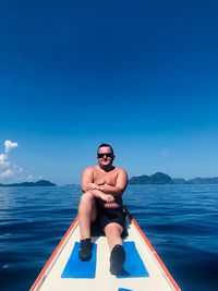 Full length of shirtless man in sea against blue sky