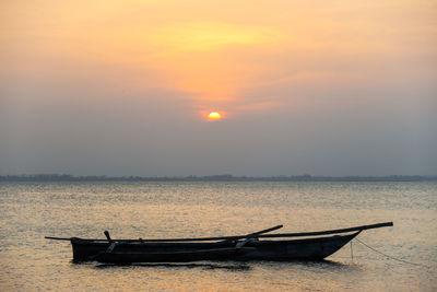 Boat moored in sea against sky during sunset