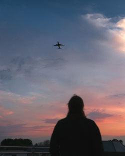Low angle view of silhouette airplane and woman against sky during sunset