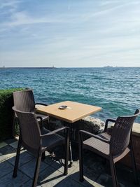 Empty chairs and table by sea against sky