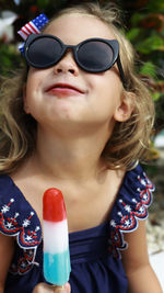 Toddler girl with blue swimsuit eating a popsicle in red, white and blue colors