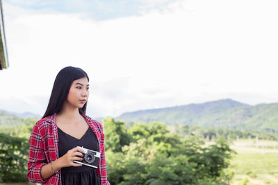 Young woman looking away while standing on mountain against sky