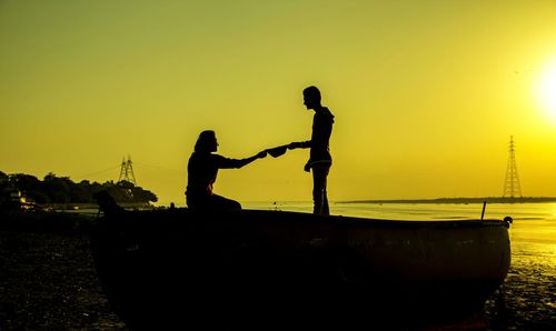 Silhouette man standing by fishing boat against clear sky during sunset