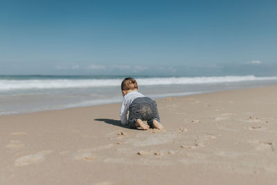 Rear view of cute boy crawling on beach
