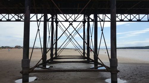 Underneath view of pier at beach against sky