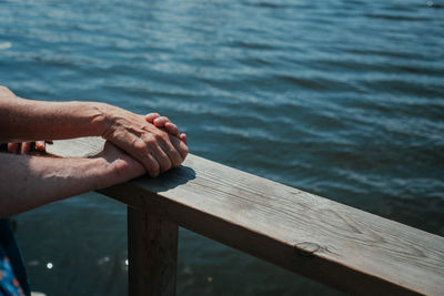 Cropped image of couple holding hands on railing against sea