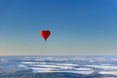 Red air balloon in the shape of heart against blue sky in a sunny day fly high above the trees
