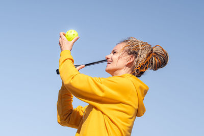 Low angle view of young woman holding apple against clear sky