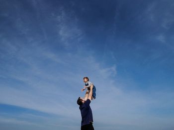 Low angle view of father playing with daughter against blue sky